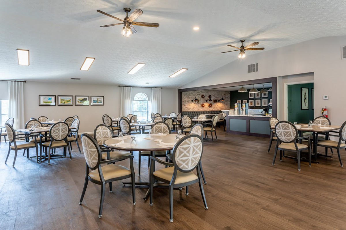 A modern dining area with multiple tables and chairs, featuring ceiling fans and decorated walls.