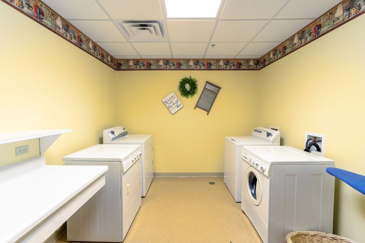 A clean and organized laundry room featuring washing machines, a dryer, and homey decorations on yellow walls.