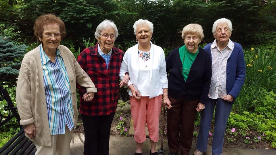 A group of elderly women smiling and holding hands in a garden.