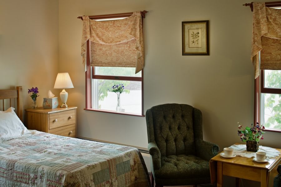 Cozy bedroom interior with a window view, featuring a bed, lamp, and armchair.