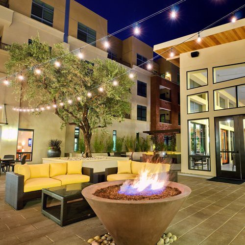 A cozy outdoor patio with string lights, a fire pit, and modern seating arrangements under the evening sky.