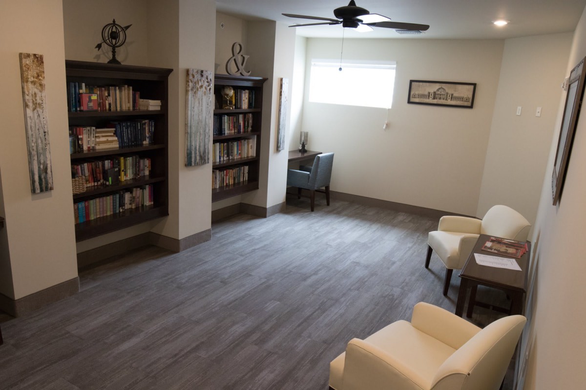A cozy library room with bookshelves, armchairs, and a reading nook by the window.