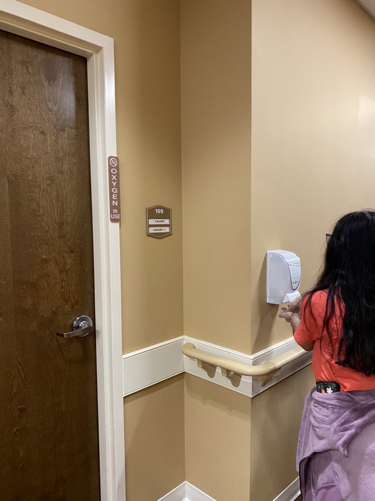 A child using a hand sanitizer dispenser in a hallway.