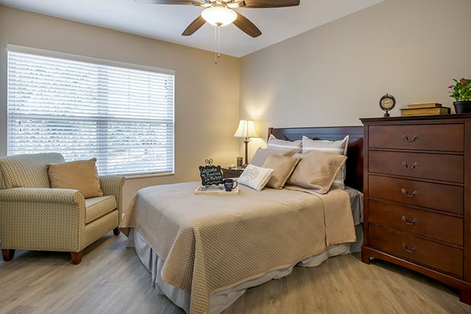 A cozy bedroom with a neatly made bed, a ceiling fan, and warm lighting.