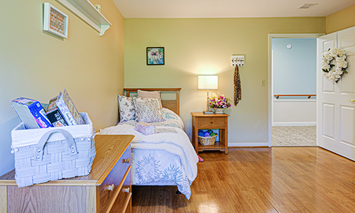A cozy bedroom with a single bed and wooden flooring, featuring a nightstand with a lamp and decorative wall art.