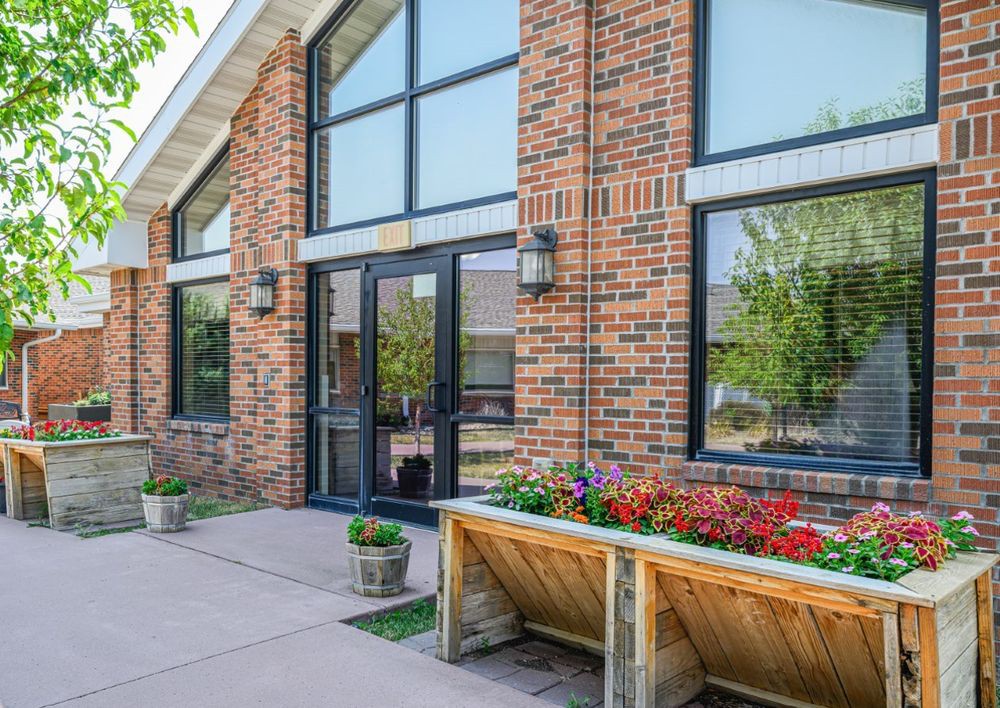A brick building with large windows and a planter filled with colorful flowers at the entrance.