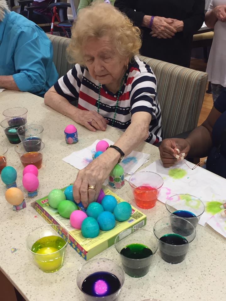 An elderly woman decorates colorful eggs during a group craft activity.