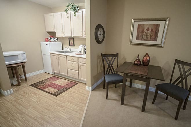A compact apartment kitchen with adjacent dining area, featuring beige cabinets, a small table, and decorative elements.
