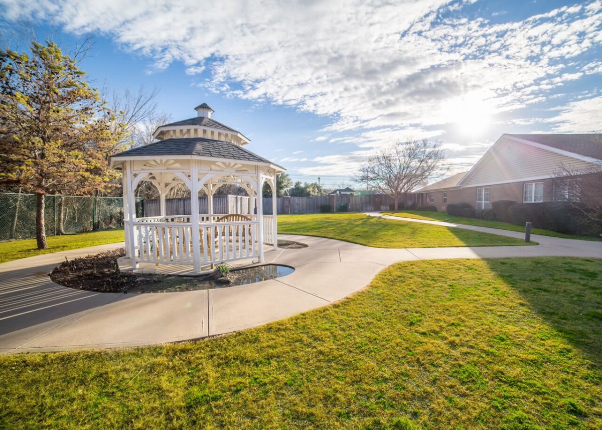 A picturesque gazebo in a sunny garden setting surrounded by green grass and a winding pathway.