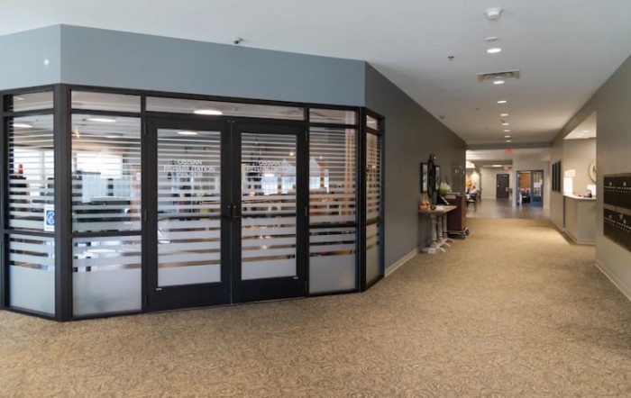 A modern office hallway with glass doors and carpeted flooring.