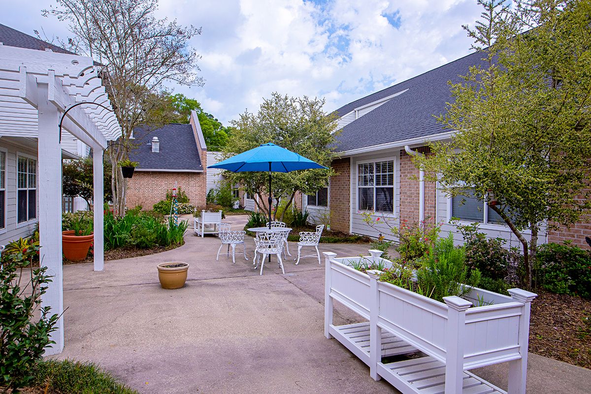 A peaceful courtyard with tables, chairs, and a blue umbrella surrounded by greenery.