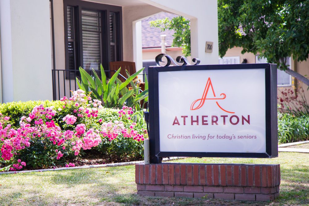 A sign for Atherton residential community surrounded by vibrant flowers and greenery.