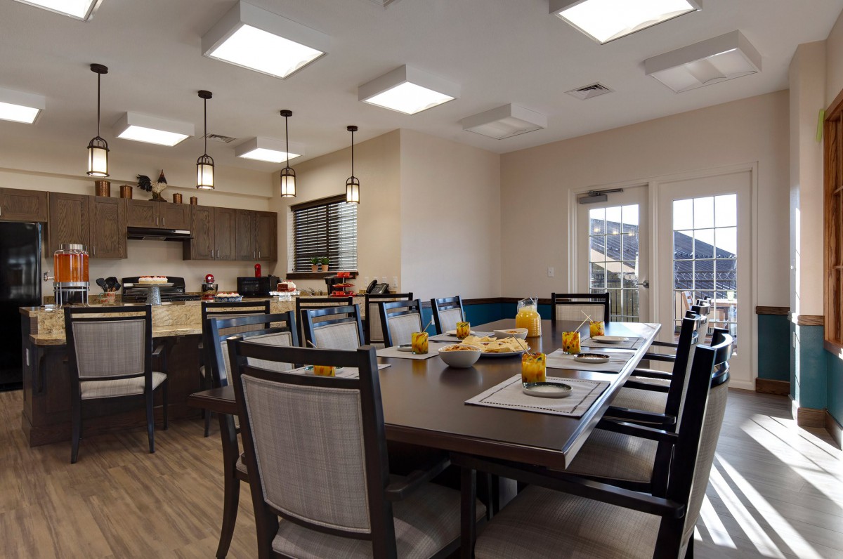 A modern dining room with a large table set for a meal, adjacent to a kitchen area.