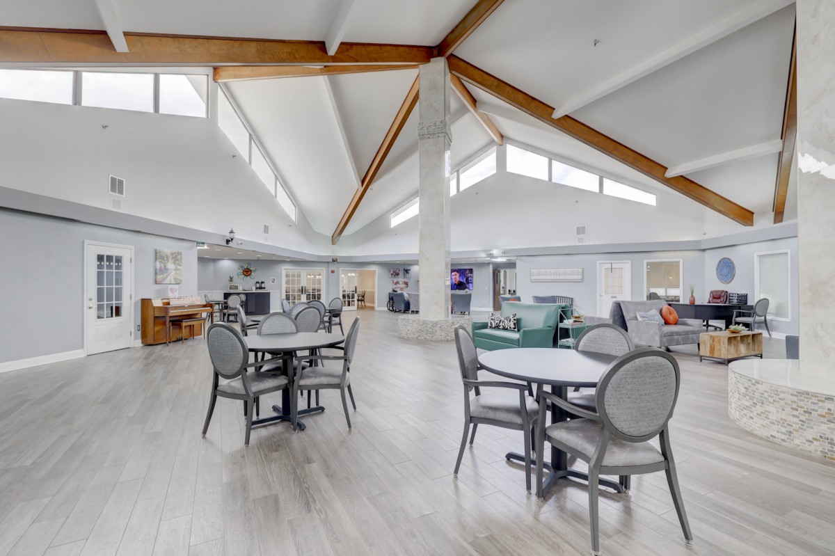 A bright and modern interior featuring a dining area with tables and chairs under high ceilings.