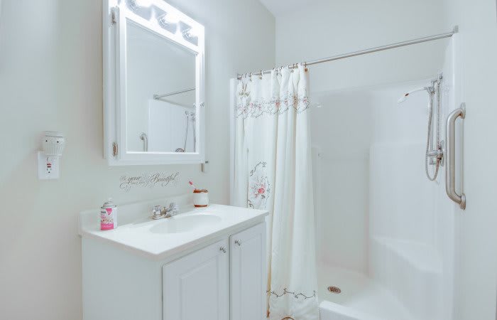 A minimalist bathroom featuring a white sink, mirror, and shower with a curtain.