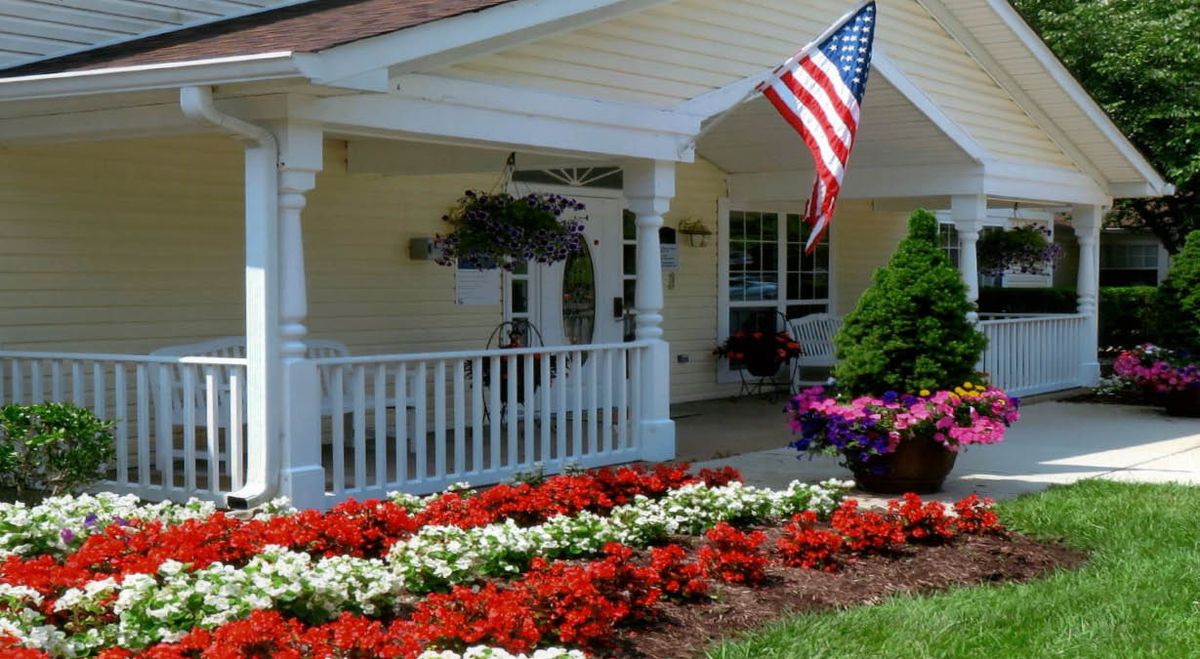A charming house with a welcoming porch, adorned by an American flag and surrounded by vibrant flower beds.