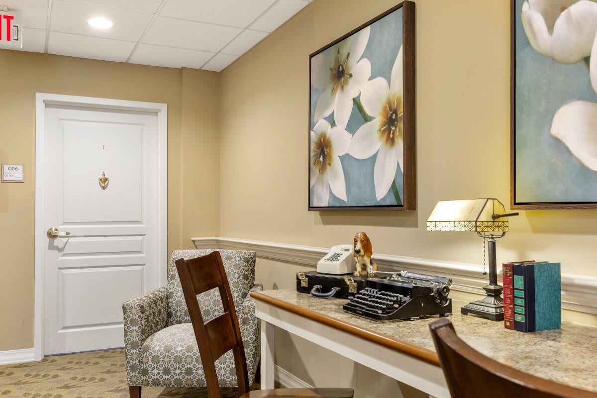 A cozy office corner with a vintage typewriter, decorated with floral artwork and a comfortable chair.