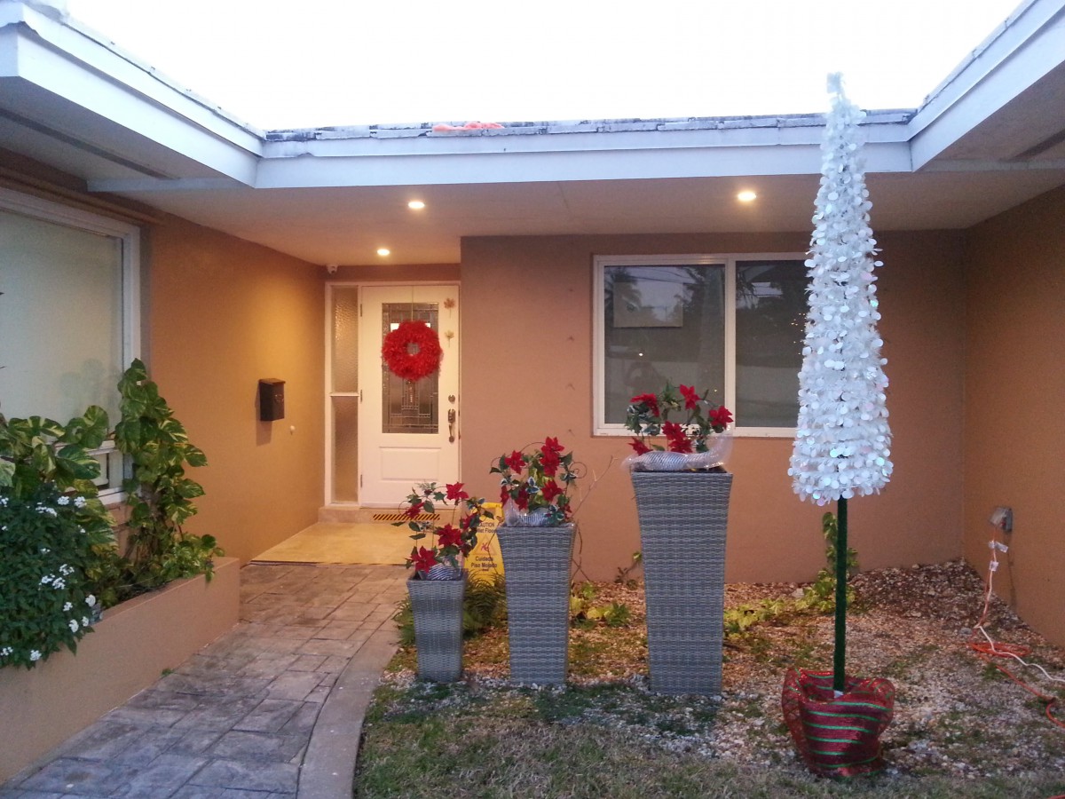 A festive house entrance with holiday decorations and potted plants.