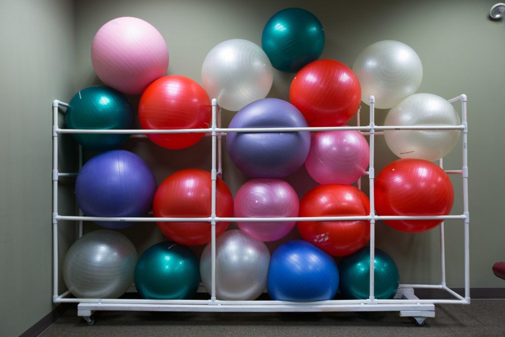 A collection of colorful exercise balls neatly arranged on a storage rack in a gym.