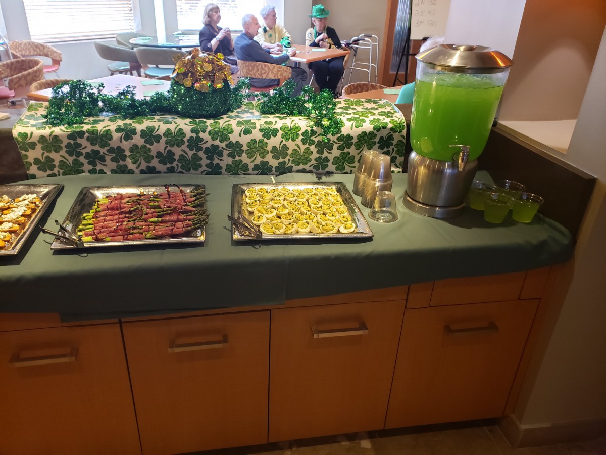 A buffet setup featuring desserts and a large container of green beverage, decorated with a green theme.