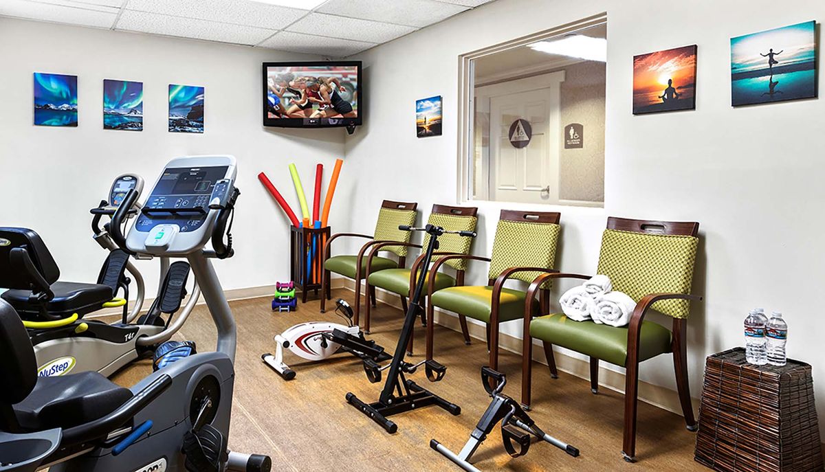 A waiting room with exercise equipment, chairs, and a wall-mounted television.