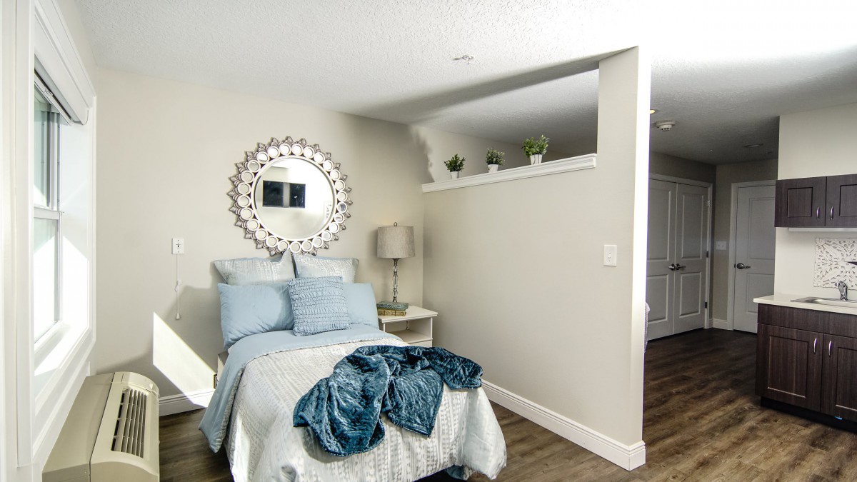 A cozy bedroom featuring a bed with blue bedding, a decorative mirror on the wall, and a modern lamp on the nightstand.