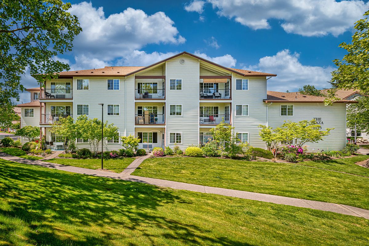 A view of a residential apartment building surrounded by greenery and a well-maintained lawn under a clear blue sky.