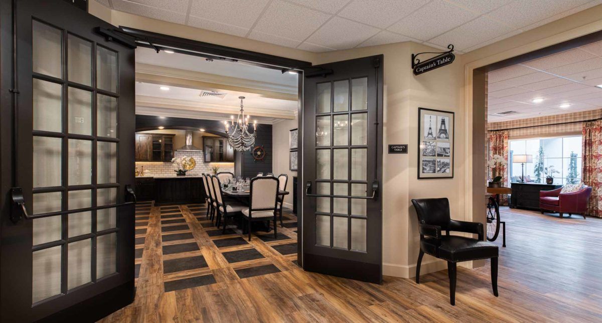 A modern dining room with a chandelier and wood flooring, visible through an open door.