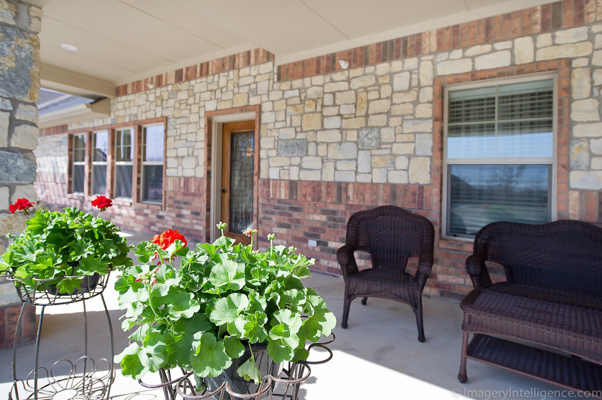 Cozy porch with wicker chairs and vibrant flowers against a stone wall backdrop.