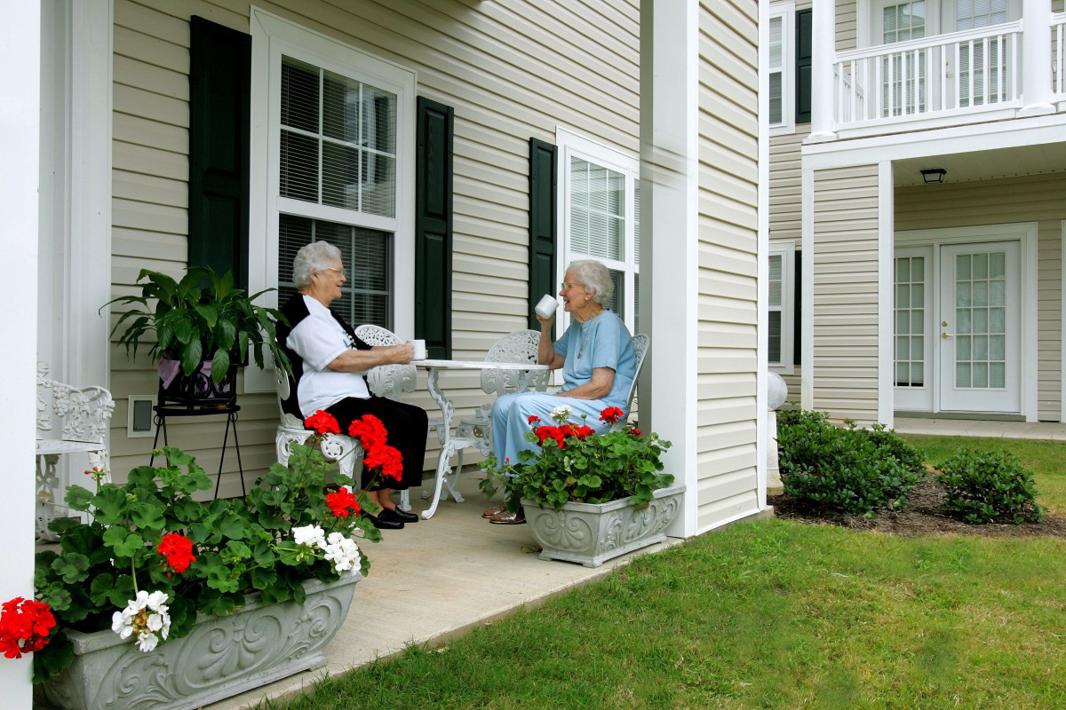 Two seniors enjoying a conversation on a patio outside a house.