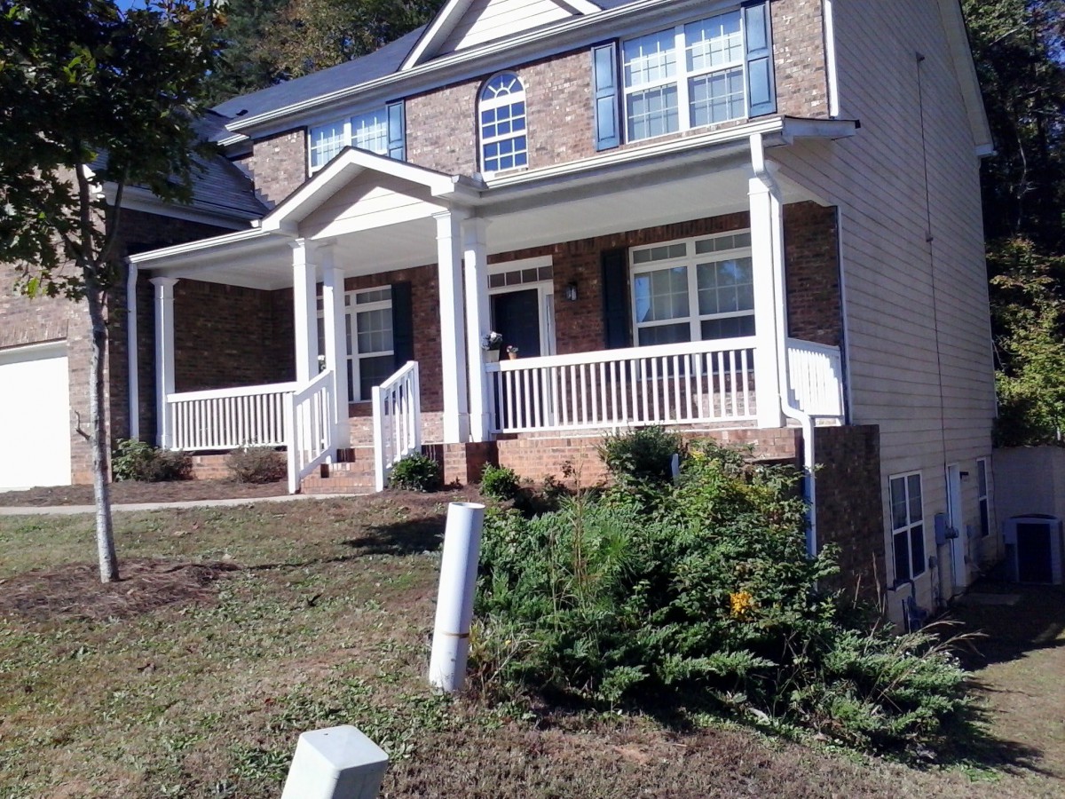A two-story suburban brick house with a front porch and landscaped yard.