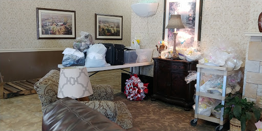 A cozy room setup featuring a table with various items, a lamp, and framed pictures on the wall.