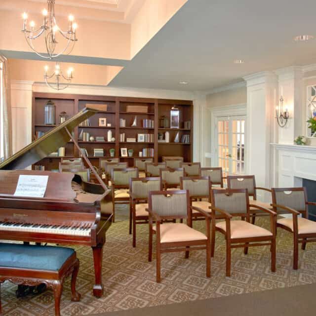 A cozy reading room featuring a grand piano and a set of arranged chairs, perfect for small gatherings or presentations.