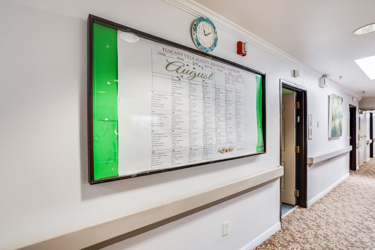 A hallway with a bulletin board displaying a schedule and a clock above.