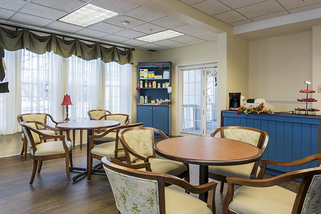 A cozy dining room with tables and chairs, featuring a window with curtains and a cabinet in the corner.