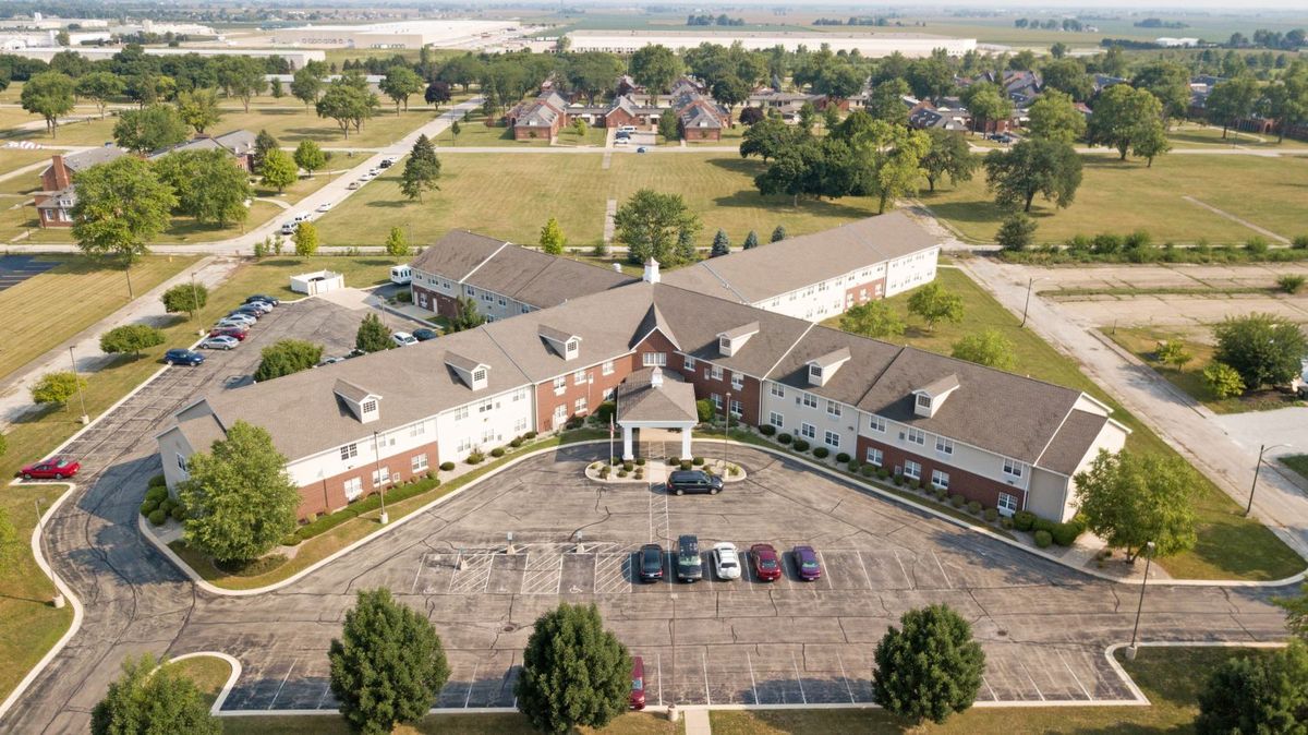 Aerial view of a large building with a parking lot surrounded by greenery in a suburban area.