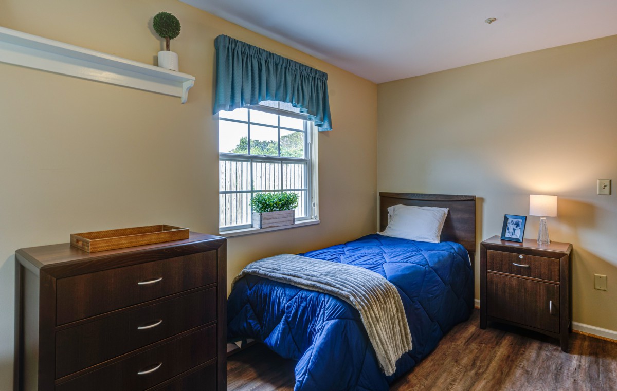 A cozy bedroom with a single bed and blue bedding, featuring wooden furniture and a window with blue curtains.