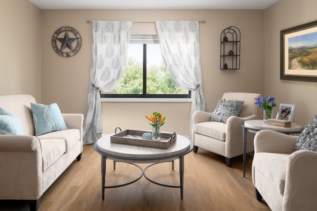 A cozy living room with a sofa, armchairs, and a coffee table in front of a window with sheer curtains.
