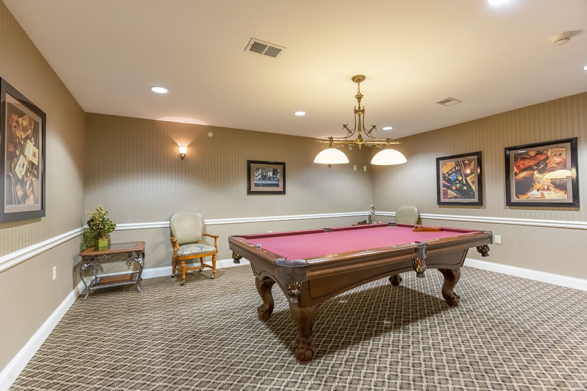 A cozy billiard room featuring a stylish pool table under a chandelier with framed artwork on the walls.