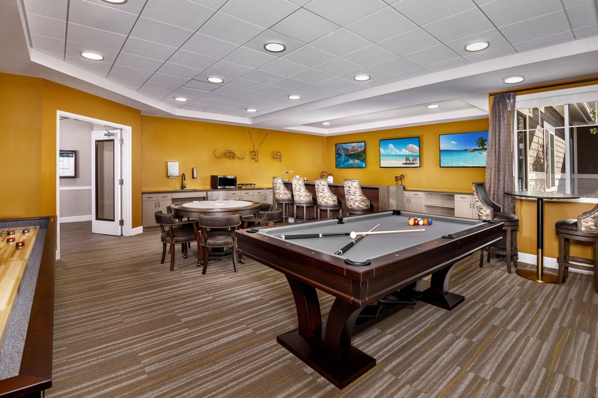 A cozy game room featuring a pool table and bar stool seating, highlighted by vibrant yellow walls and decorative paintings.