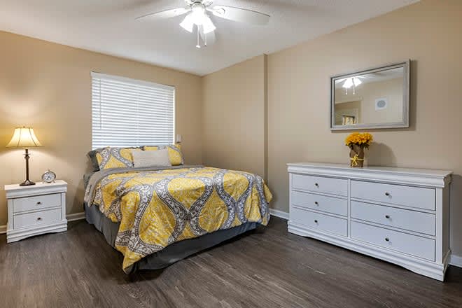 A cozy bedroom with yellow bedding and simple decor, featuring a dresser and mirror.