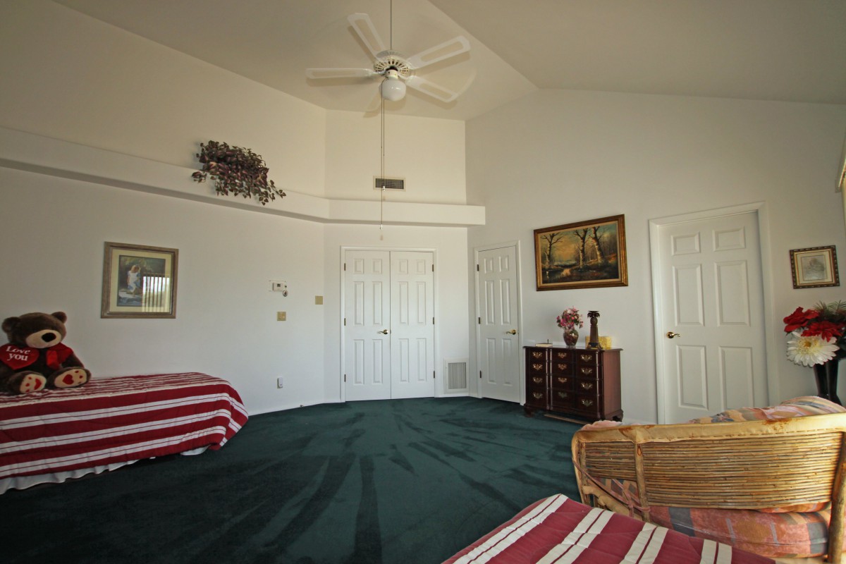 A spacious bedroom with green carpet, featuring striped bedding and classic wooden furniture.