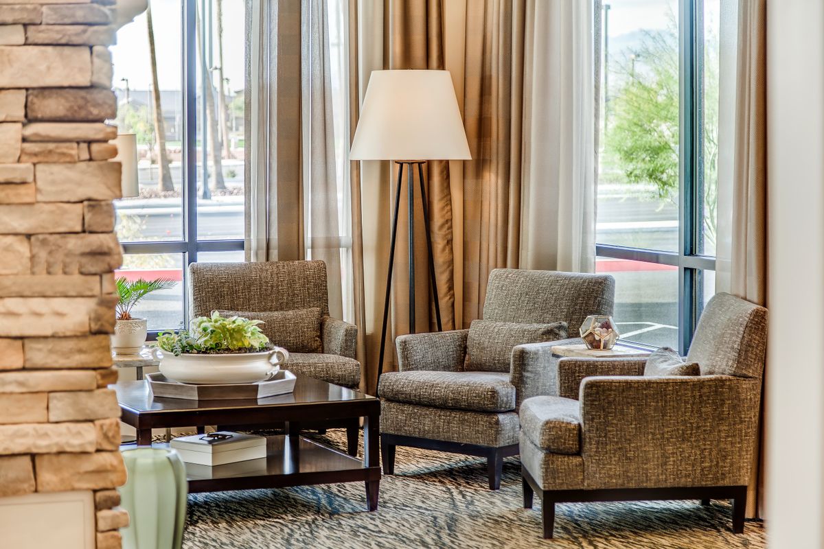 A cozy living room setup featuring comfortable chairs, a floor lamp, a coffee table with decor, and large windows with curtains.