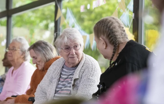 An elderly woman and a young person engaging in conversation indoors.
