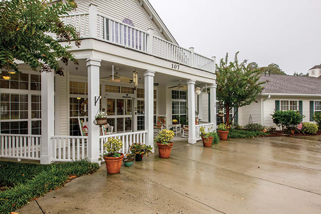 A charming white house with a porch and potted plants on a rainy day.