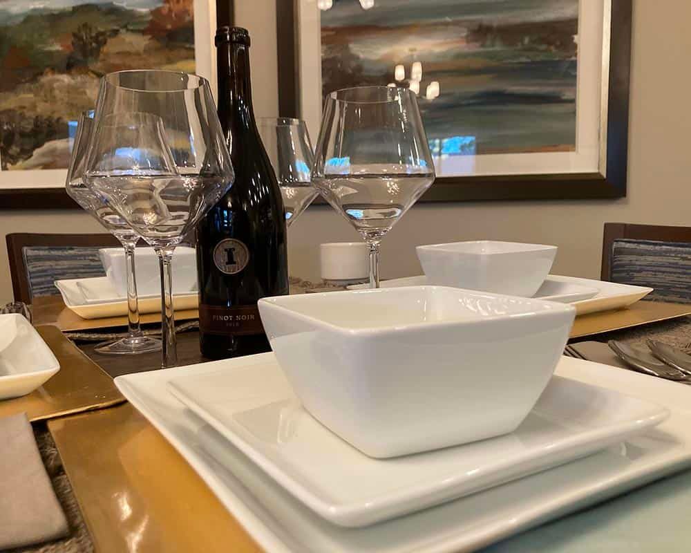 A beautifully arranged dining table with elegant white dishware and a bottle of wine.