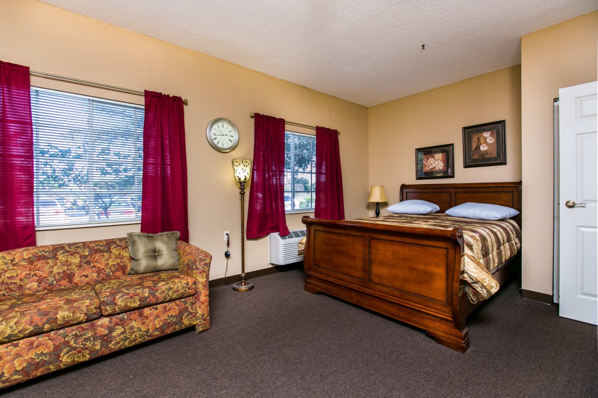A cozy bedroom featuring a wooden bed, floral couch, and vibrant red curtains.