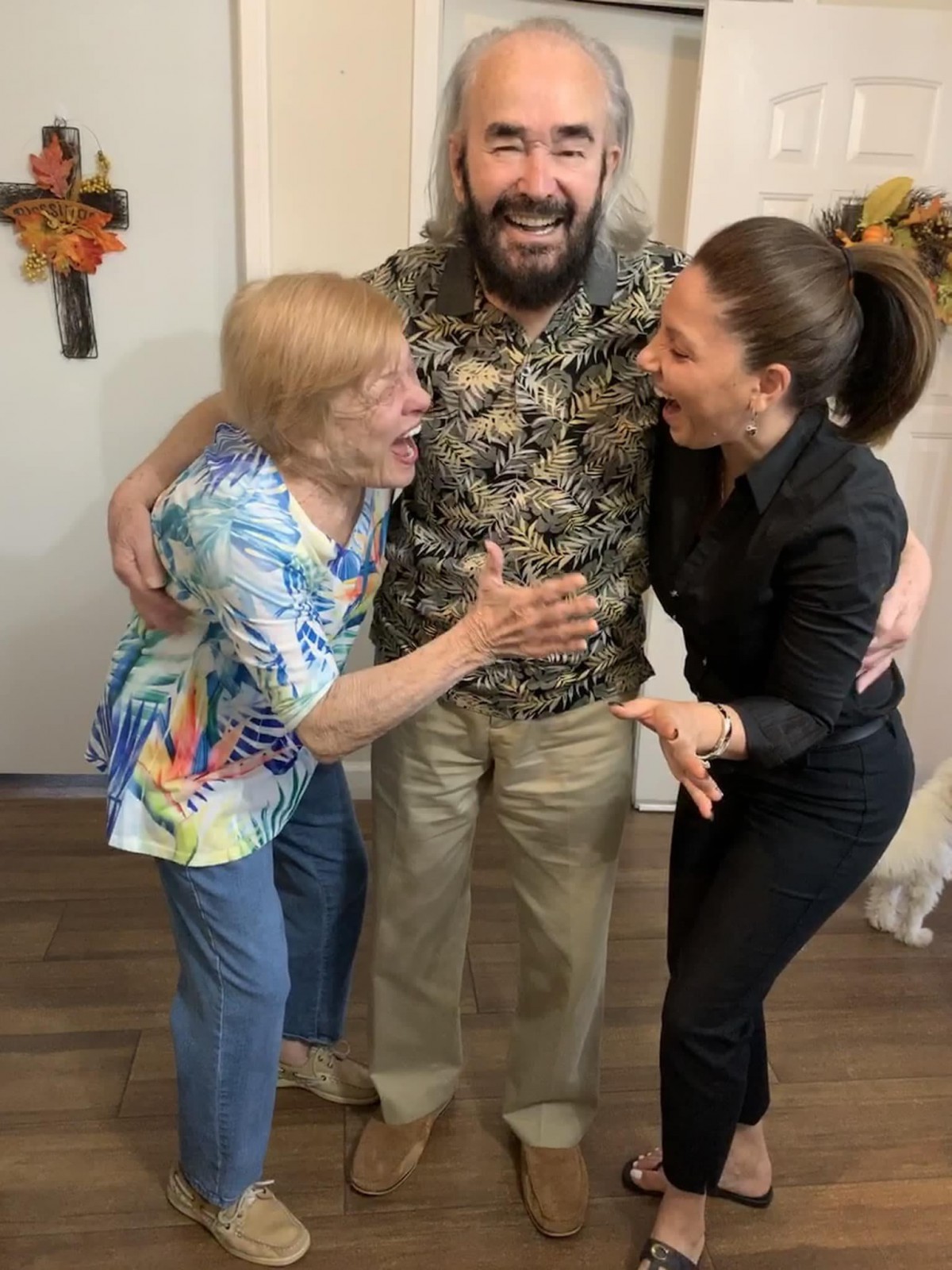 Three people joyfully embrace indoors, sharing a moment of laughter.