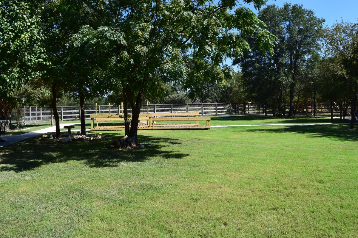 A peaceful park scene with lush green grass, trees, and a wooden fence.