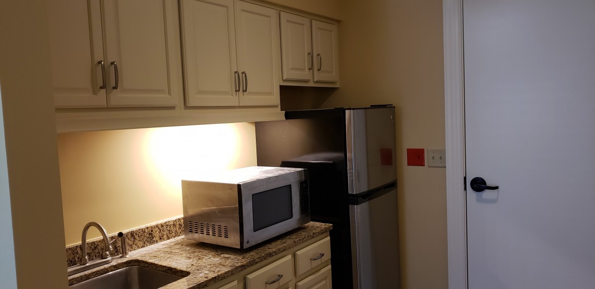 A small kitchen area with a microwave, refrigerator, and cabinets.